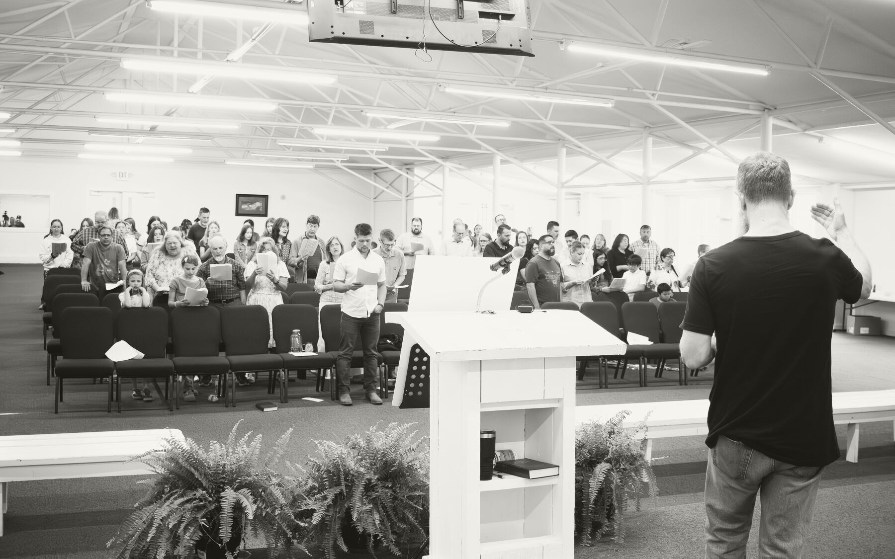 The congregation standing to sing together while a man leads from a simple wooden podium.